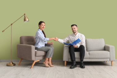 Human resources manager with applicant shaking hands near green wall in office