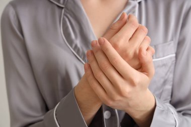 Süslü pijamalı bir kadın ellerine krem sürüyor.