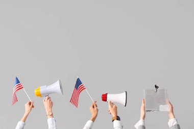 Eller oy sandığını tutuyor, beyaz arka planda Amerikan bayrakları ve megafonları var. Seçim kavramı