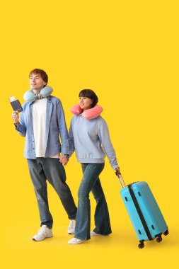 Sarı arka planda yürüyen pasaport ve bavullu iki genç turist.