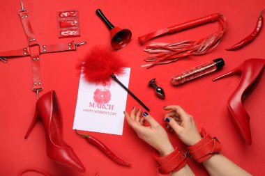 Farklı seks oyuncakları olan kadın elleri, kırmızı arka planda tebrik kartı ve prezervatifler. Uluslararası Kadınlar Günü kutlamaları