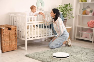 Küçük bebeği beşiğinde ve robot elektrikli süpürgesiyle evde oturan genç bir kadın.