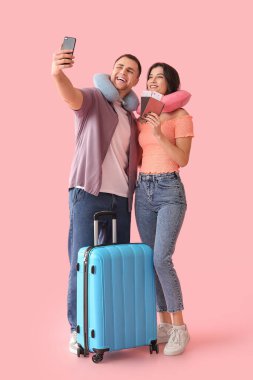 Güzel, genç, mutlu, bavulları, pasaportları ve biletleri olan turistler pembe arka planda selfie çekiyorlar.