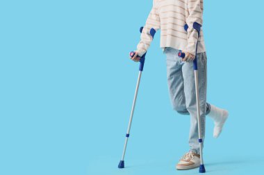 Mavi arka planda koltuk değnekleriyle kazadan sonra yaralanan genç kadın.