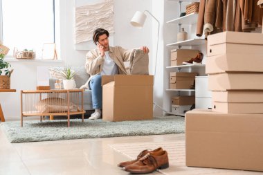 Giysi kutuları ve şık giysileri olan yakışıklı genç adam soyunma odasında cep telefonuyla konuşuyor.