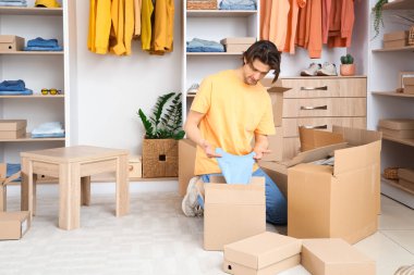 Yakışıklı genç adam soyunma odasında şık giysileri olan kıyafet kutularını açıyor.