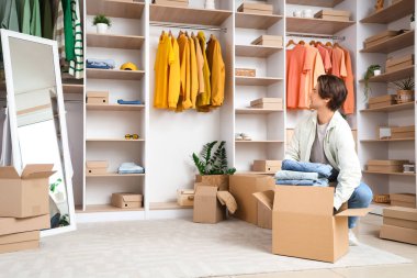 Yakışıklı genç adam soyunma odasında şık kotlarla dolu kıyafet kutularını açıyor.