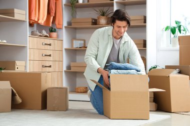 Yakışıklı genç adam soyunma odasında şık kotlarla dolu kıyafet kutularını açıyor.