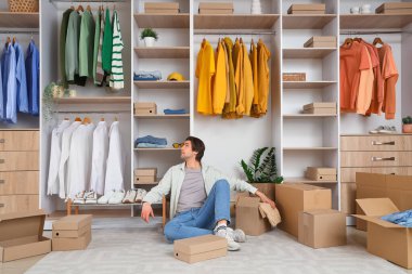 Soyunma odasında kostüm kutuları ve şık giysileri olan yakışıklı, yorgun bir adam.