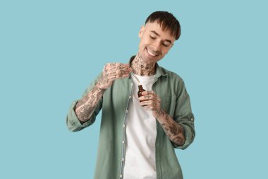 Mavi arka planda bir şişe CBD yağı olan dövmeli genç bir adam.