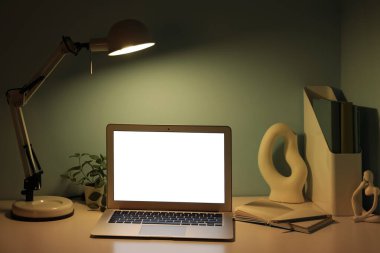 Modern dizüstü bilgisayarı, heykeli ve yeşil duvarın yanında parlayan lambası olan işyeri