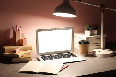 Modern dizüstü bilgisayarı, bir fincan kahvesi, kitapları ve pembe duvarın yanında parlayan lambası olan bir yer.