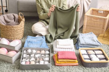 Kadın, yerde otururken temiz giysileri organizatörlerle katlıyor.