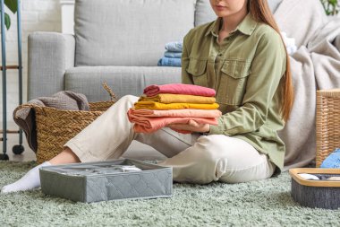 Kadın, yerde otururken temiz giysileri organizatörlerle katlıyor.