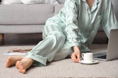 Bir fincan kahve ve dizüstü bilgisayarla halıda dinlenen bir kadın. Yakın çekim.