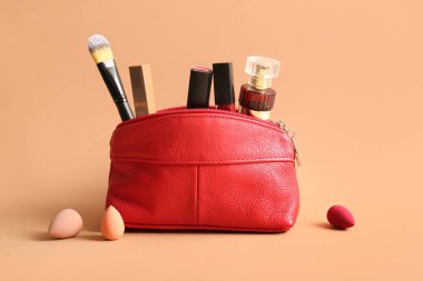 Kırmızı makyaj çantası, ruj, parfüm şişesi ve bej arka planda makyaj malzemeleri.