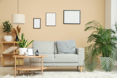 Rahat kanepesi, çiçekleri ve bej duvarında boş resim çerçeveleri olan şık bir oturma odası.