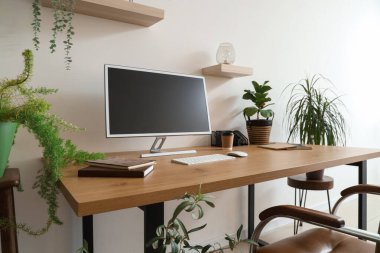 Ofis duvarının yanında bilgisayar monitörü ve ev bitkileri olan modern işyeri