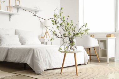 Kahve masasının üzerinde çiçekli bir vazo, rahat bir yatak odası ve beyaz yatak odasının yanında.