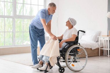 Evde kemoterapiden sonra karısını tekerlekli sandalyeyle örten ekoseli olgun bir adam.