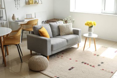 Oturma odasındaki kahve masasında nergis çiçekleri olan rahat bir kanepe ve vazo.