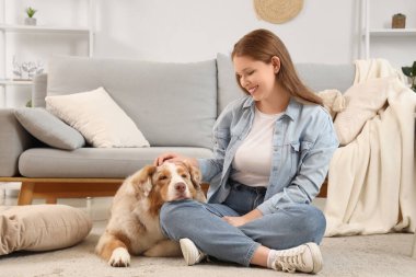 Şirin bir Avustralya çoban köpeği olan genç bir kadın evde yerde oturuyor.