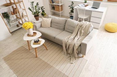 Oturma odasında, kahve masasında gri kanepe ve sarı narsisli çiçekler var.