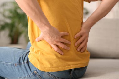 Handsome young man suffering from back pain at home, closeup