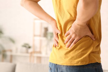 Handsome young man suffering from back pain at home, closeup