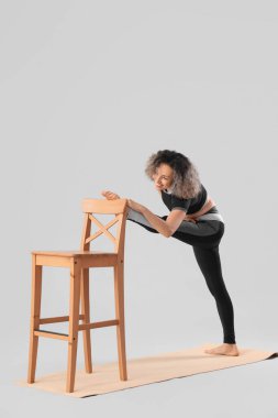 Sandalyesi olan sportif olgun bir kadın hafif arka planda yoga yapıyor.