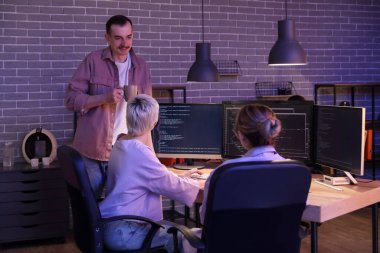 Kahve içen bir erkek programcı ve geceleri ofiste çalışan meslektaşları.