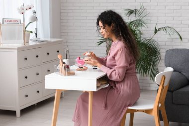 Güzel, mutlu, Afro-Amerikan bir kadın evde makyaj yaparken pudra sürüyor.