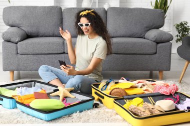 Güzel, genç ve mutlu bir kadın selfie çekiyor ve evdeki bavullardan yaz kıyafetlerini çıkarıyor.