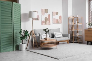 Oturma odasının içinde rahat bir kanepe, sehpa ve beyaz duvarda resimler var.