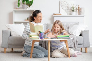 Evde küçük bir kıza kitap dersi veren kadın öğretmen.