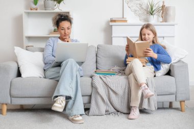 Kitaplı ve özel öğretmenli küçük kız evdeki kanepede ders çalışıyor.