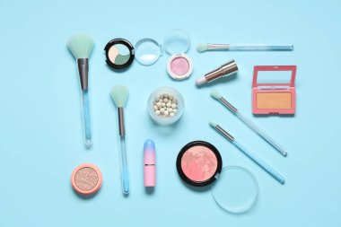 Mavi zemin üzerinde kozmetik ürünler bulunan şık makyaj fırçaları
