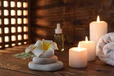 Plumeria çiçekli spa taşları ve ahşap masada parlayan mumlar.