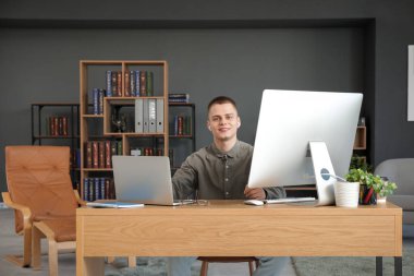 Genç erkek serbest bilgisayar ve dizüstü bilgisayarla modern ev ofisinde çalışıyor.