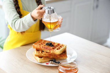 Mutfaktaki waffle 'ların üzerine bal döken tatlı küçük kız, yakın plan.