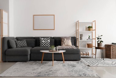 İçinde siyah kanepe, sehpa, saksı ve raf ünitesi olan güzel bir oturma odası.