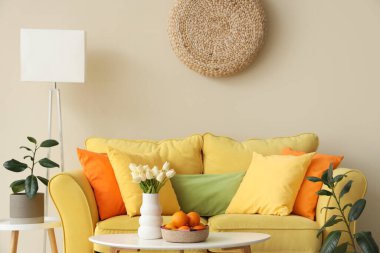 Sarı kanepeli güzel oturma odasının içi, sepetin içinde kahve masasının üzerinde meyve vazosu olan laleler.