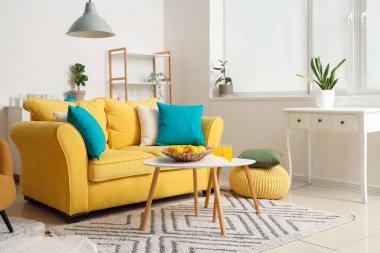 İçinde sarı kanepe, sehpa, yastıklar ve raf ünitesi olan güzel bir oturma odası.