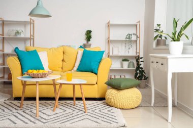 İçinde sarı kanepe, sehpa, yastıklar ve raf ünitesi olan güzel bir oturma odası.