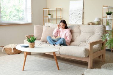 Kitap okuyan ve evdeki kanepede oturan güzel genç bir kadın.