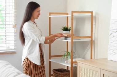 Güzel genç bir kadın evdeki raflardan kitap alıyor.