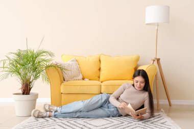 Güzel genç bir kadın kitap okuyor ve evde yerde yatıyor.