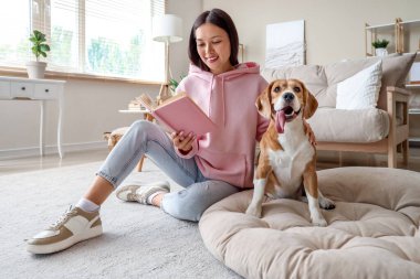 Oturma odasında yerde sevimli bir tazı köpeğiyle kitap okuyan genç bir kadın.