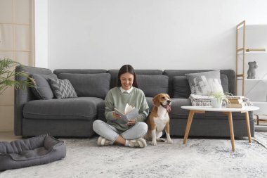 Genç bir kadın kitap okuyor ve oturma odasında yerde sevimli bir tazı köpeğiyle oturuyor.