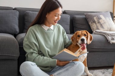 Genç bir kadın kitap okuyor ve oturma odasında yerde sevimli bir tazı köpeğiyle oturuyor.